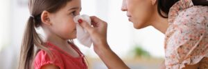 mom holding tissue to child nose