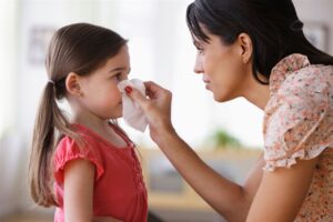 mom holding tissue to child nose